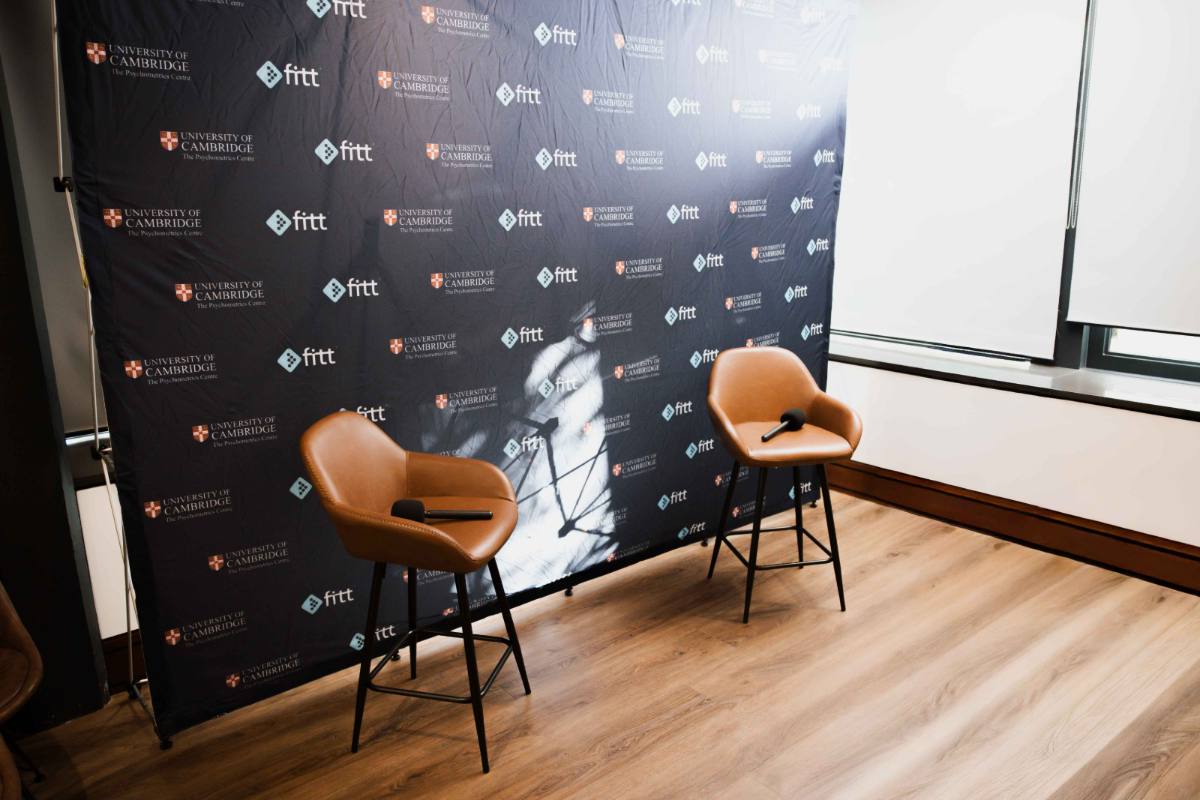 Interview set with two leather stools in front of a University of Cambridge and Fitt branded backdrop.