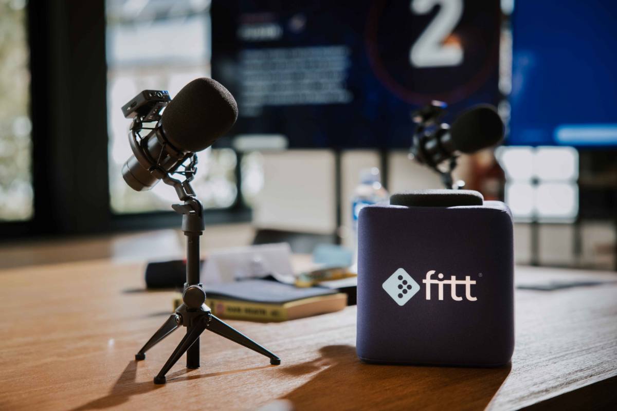 Podcast microphones and a Fitt-branded windscreen set up on a wooden table.