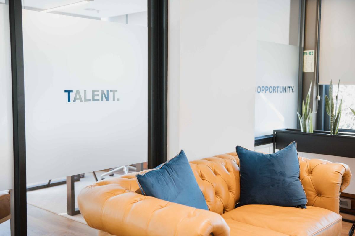 A tan tufted leather couch beside frosted-glass panels reading &lsquo;Talent.&rsquo; and &lsquo;Opportunity.&rsquo;